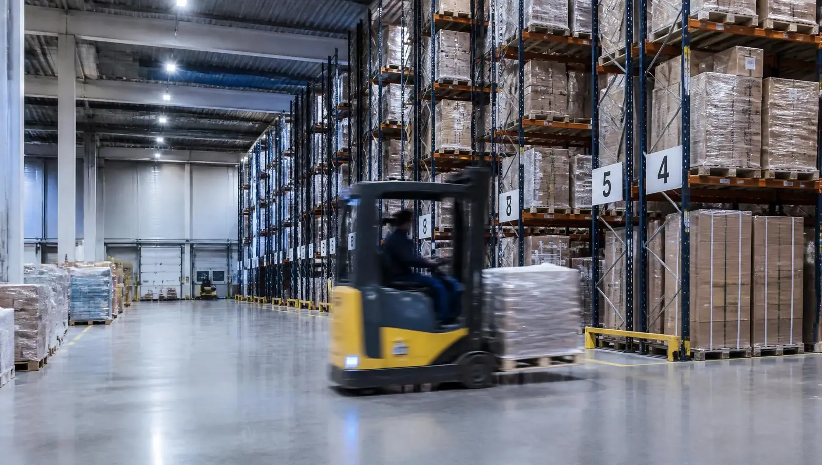 Distribution warehouse with palletised goods and forklift in motion